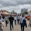 Illustrative photo of commuters dressed in hoodies and light jackets walking through Accra's central business district under heavy grey clouds during Ghana's unusually cool weather.