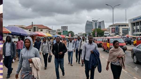 Illustrative photo of commuters dressed in hoodies and light jackets walking through Accra's central business district under heavy grey clouds during Ghana's unusually cool weather.